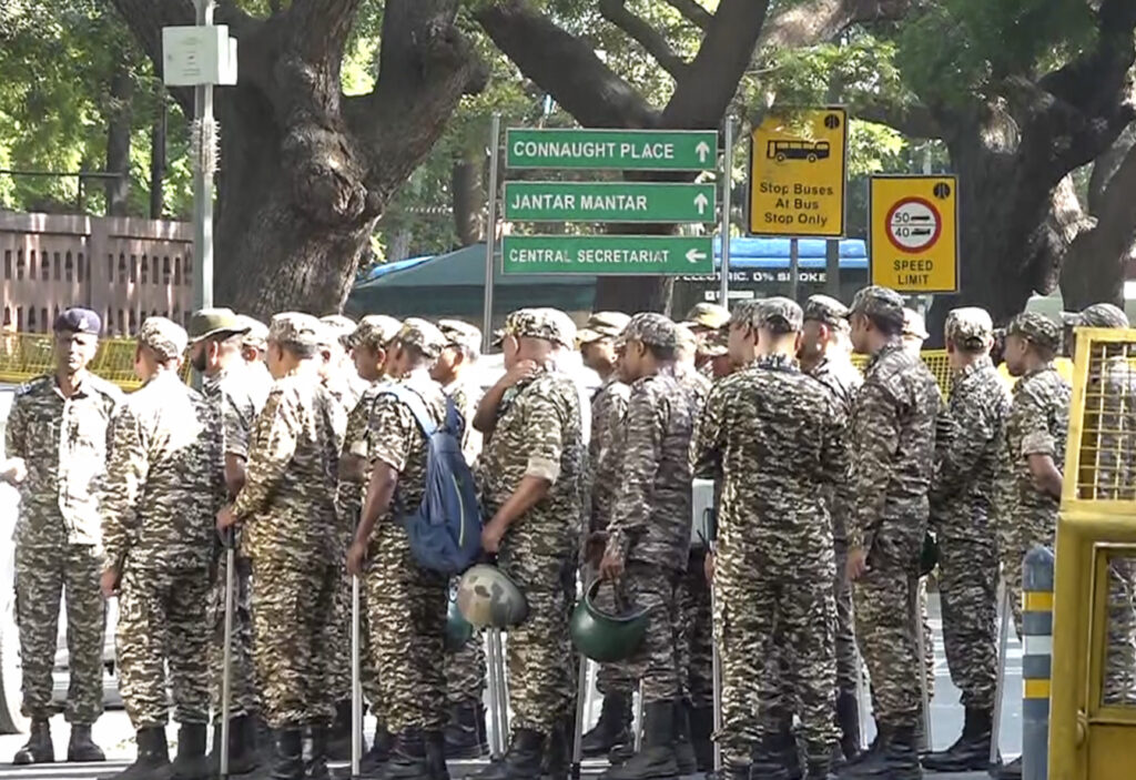 Indian police officers in camouflage uniforms standing in a line during a protest or event.