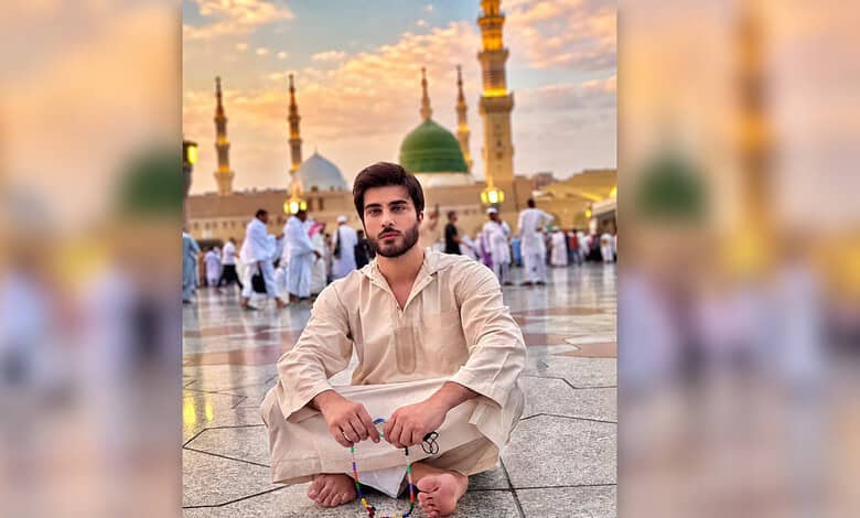 Imran Abbas sitting cross-legged at a mosque with minarets and a green dome in the background.