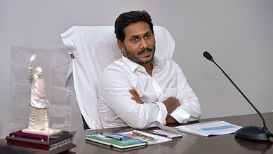 Man in white shirt sitting at desk with crossed arms in office setting.