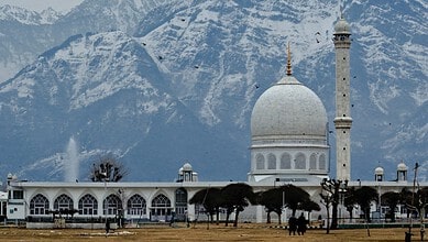 White mosque with dome and minaret against snow-capped mountains in Kashmir.