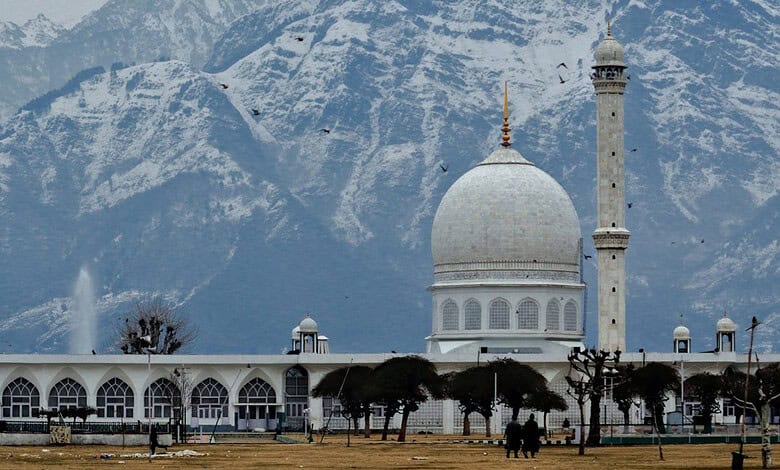 White mosque with dome and minaret against snow-capped mountains in Kashmir.
