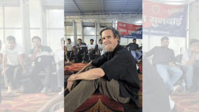 Jean Drèze sitting on the ground during a protest with others in the background.