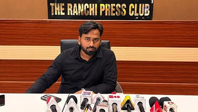 Man in black shirt at press conference with microphones in front, 'The Ranchi Press Club' sign behind.