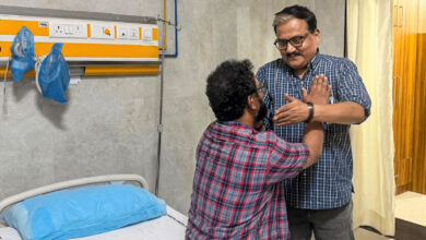 Two men in a hospital room, one sitting on the bed and the other standing, engaging in a conversation.