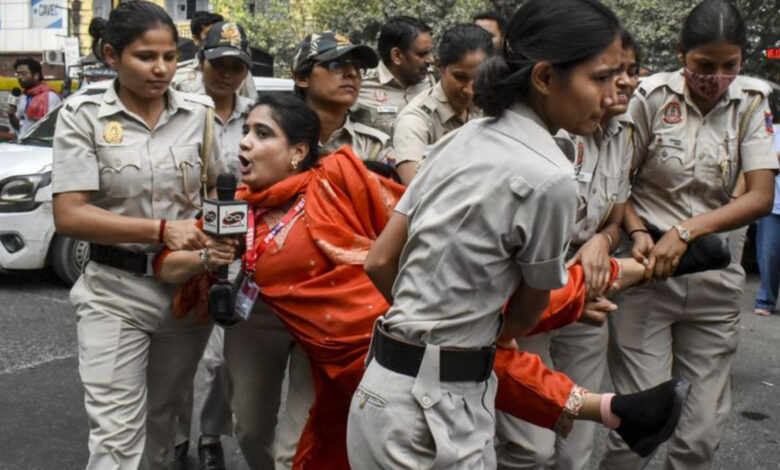 Police detain a woman during a protest, surrounded by officers in uniform on a city street.
