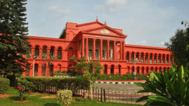 Historic red building with classical architecture and lush greenery in front.