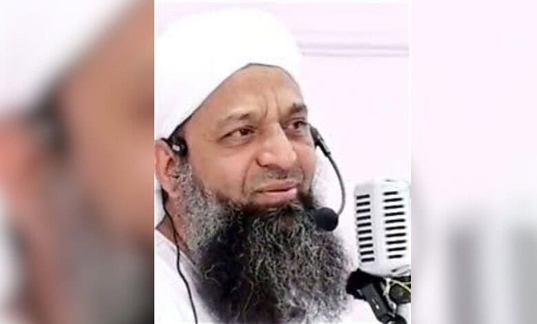 Close-up of a Muslim preacher with a white turban and beard speaking into a microphone.