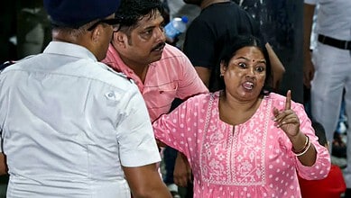 Woman in pink saree gesturing during a discussion at a crowded event.