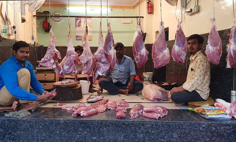 Meat shop with hanging cuts of meat and three men sitting on the floor.