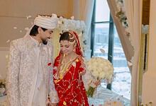 Indian bride and groom in traditional wedding attire smiling indoors.