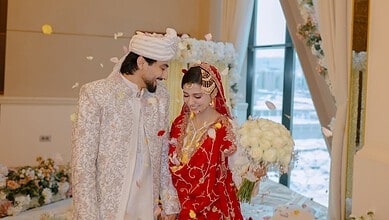 Indian bride and groom in traditional wedding attire smiling indoors.