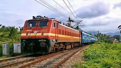 Passenger train moving through lush green landscape near Mysuru during daytime.