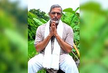 Nana Patekar praying outdoors with greenery in the background.