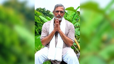 Nana Patekar praying outdoors with greenery in the background.