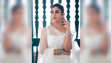 Nayanthara wearing a white saree with jewelry, posing thoughtfully indoors.