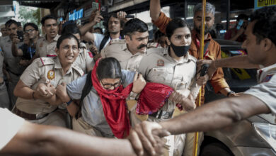 Police officers and a woman in a red scarf involved in a heated confrontation at a busy location.