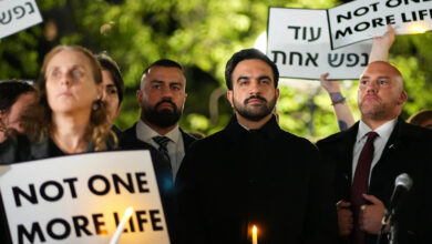 Mamdani at vigil with protesters holding signs for life and peace, night scene.