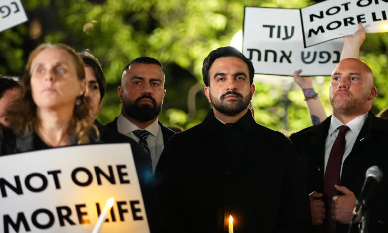 Mamdani at vigil with protesters holding signs for life and peace, night scene.