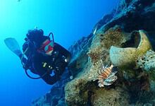 Diver exploring an ancient shipwreck off the coast of Turkey with a lionfish nearby.