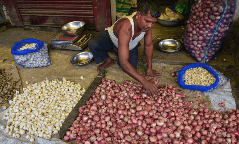 Man sorting onions at a market stall with various onion types displayed.