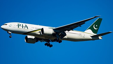 Pakistan International Airlines plane flying in clear blue sky.