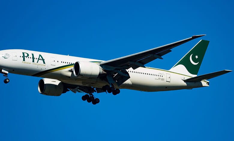 Pakistan International Airlines plane flying in clear blue sky.