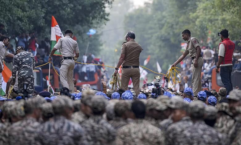 Police and security personnel at a protest rally with a large crowd and flags in Delhi.