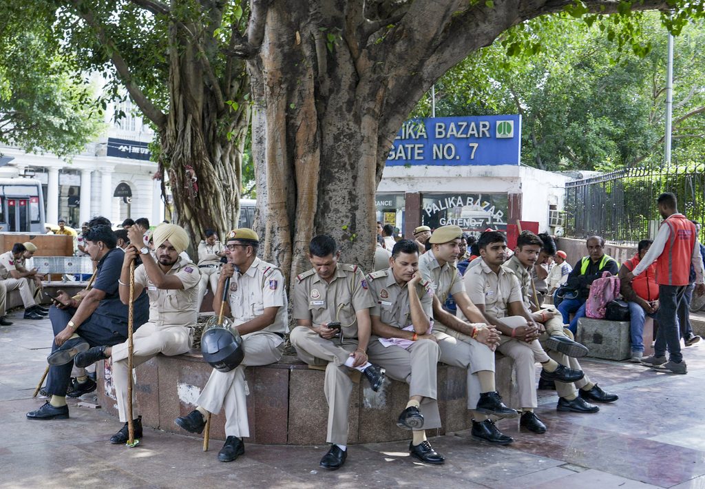 Group of police officers sitting under a large tree in a busy public area in India.