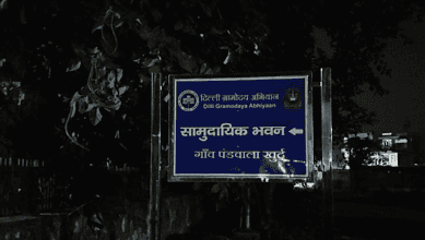 Blue signboard with white text and symbols in Hindi and English at night.