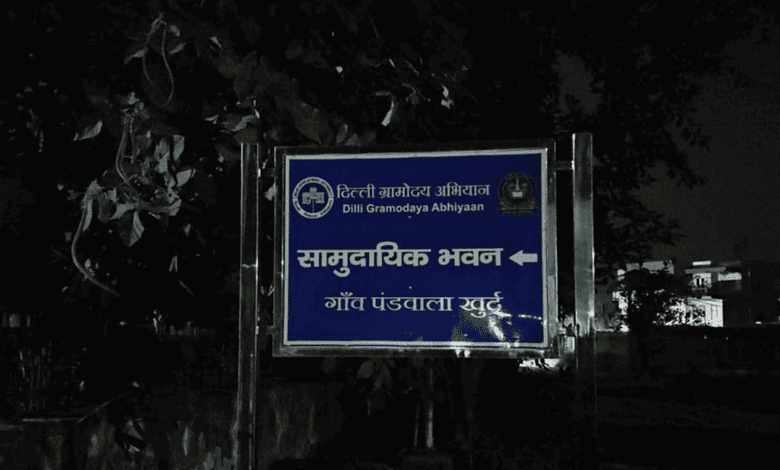 Blue signboard with white text and symbols in Hindi and English at night.