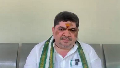 Ponnam Prabhakar wearing a white shirt and a green scarf, sitting indoors with a neutral background.