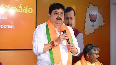 Telangana BJP chief speaking at a political event with party symbols and leaders in the background.