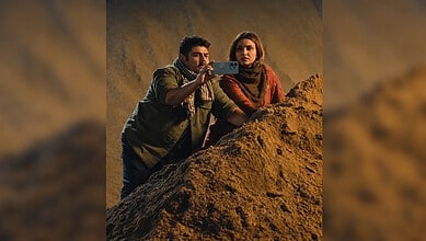 Two actors filming a scene on a rocky set for a drama production.