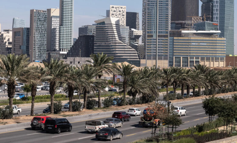 View of Riyadh skyline with tall modern buildings and palm-lined streets in the foreground.