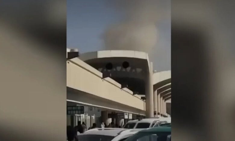 Smoke rising from a building after an incident, with parked cars in the foreground.