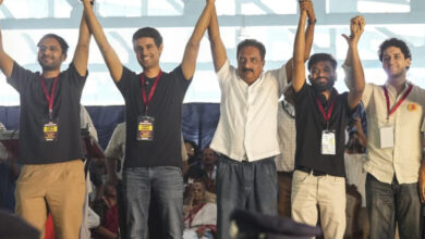 Group of men celebrating on stage at an event, holding hands raised in victory.