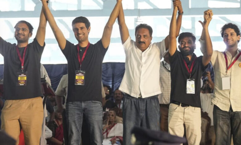 Group of men celebrating on stage at an event, holding hands raised in victory.