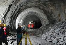 Workers and machinery inside a large underground mining tunnel under construction.