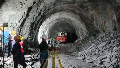 Workers and machinery inside a large underground mining tunnel under construction.