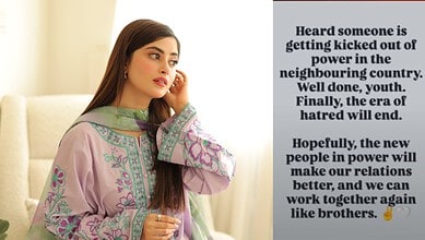 Pakistani woman in traditional dress looking thoughtfully, with a background of a beige sofa and a wall.