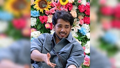 Young man smiling in front of a colourful flower wall, possibly related to Bigg Boss 20 mystery girl.