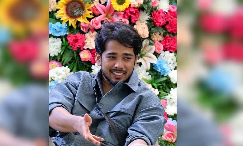 Young man smiling in front of a colourful flower wall, possibly related to Bigg Boss 20 mystery girl.