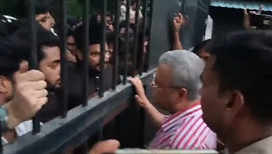 Protest at AMU with students blocking gates and an elderly woman engaging with them.