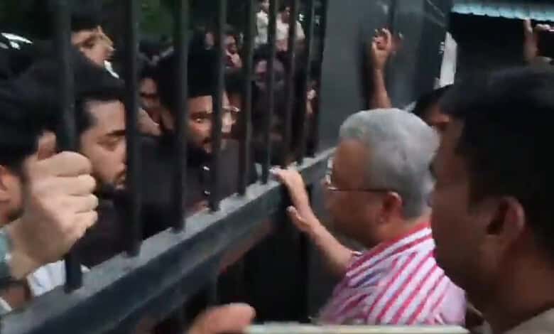 Protest at AMU with students blocking gates and an elderly woman engaging with them.