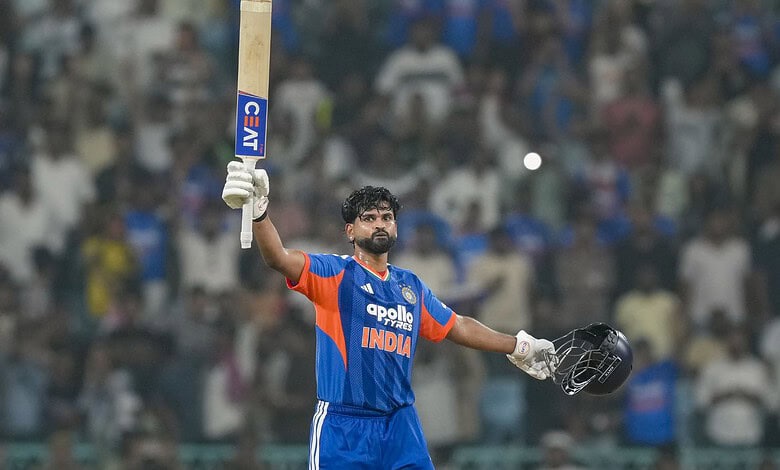 Indian cricket player in blue jersey holding bat and helmet on the field.