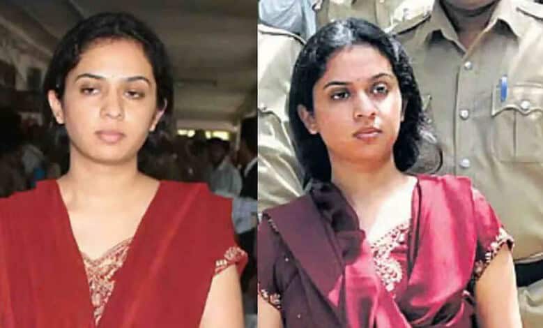 Two women in sarees at a public event, one in red and the other in maroon, with serious expressions.
