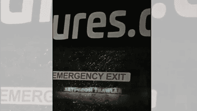 Emergency exit sign on a bus with water droplets, dark background, and partial website text.