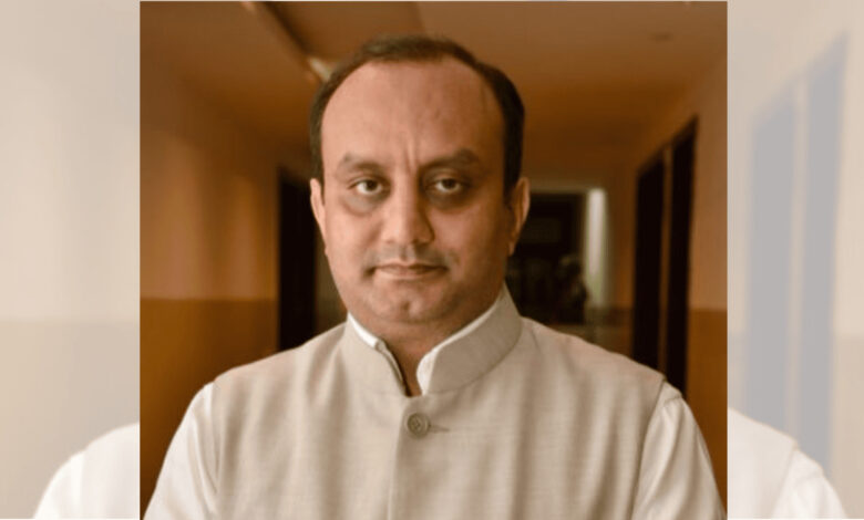 Indian man in traditional attire with a neutral expression, indoor setting.