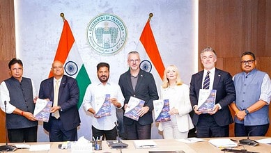 Telangana government officials and UK delegation members at a signing event with flags and documents.