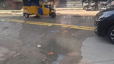 Street scene with auto rickshaw, motorcycles, and cars on a wet road in India.